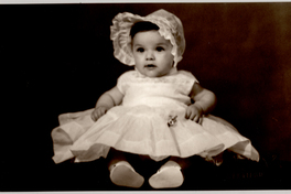 [Bebé sentada con un vestido muy amplio color blanco y un sombrero del mismo color y chalas]
