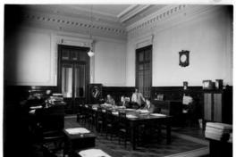 [Biblioteca Nacional 1927. Salones interiores, con una mesa rectangular y cuatro personas]